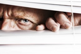 Frowning man peeps through venetian blinds